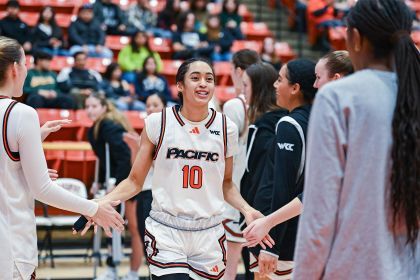 A Pacific women's basketball player high fives other players on the basketball court.